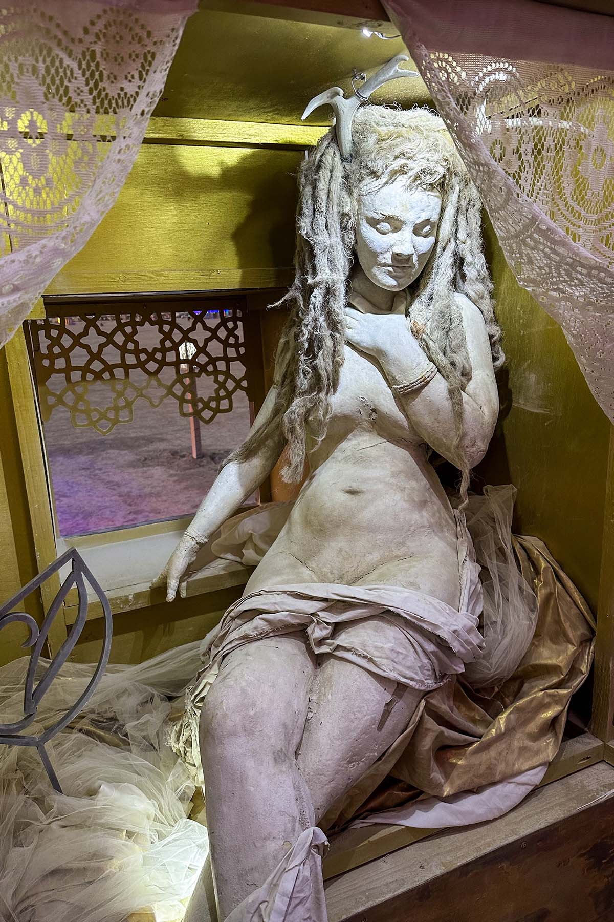 Sculpted woman with long braided hair seated in a golden alcove, partly draped in fabric
