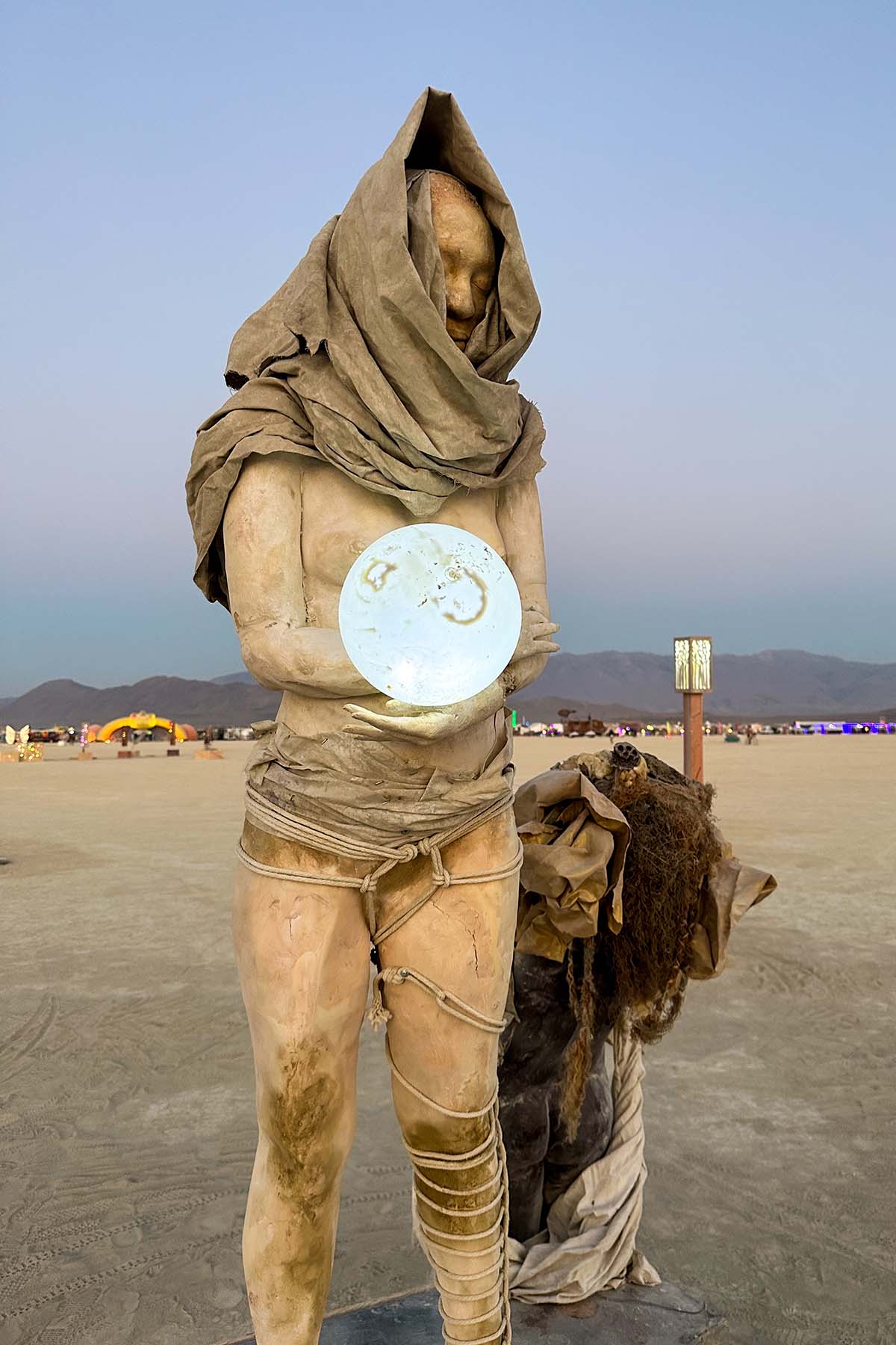 Hooded figure holding a white orb, with a crouching fur-covered figure behind it