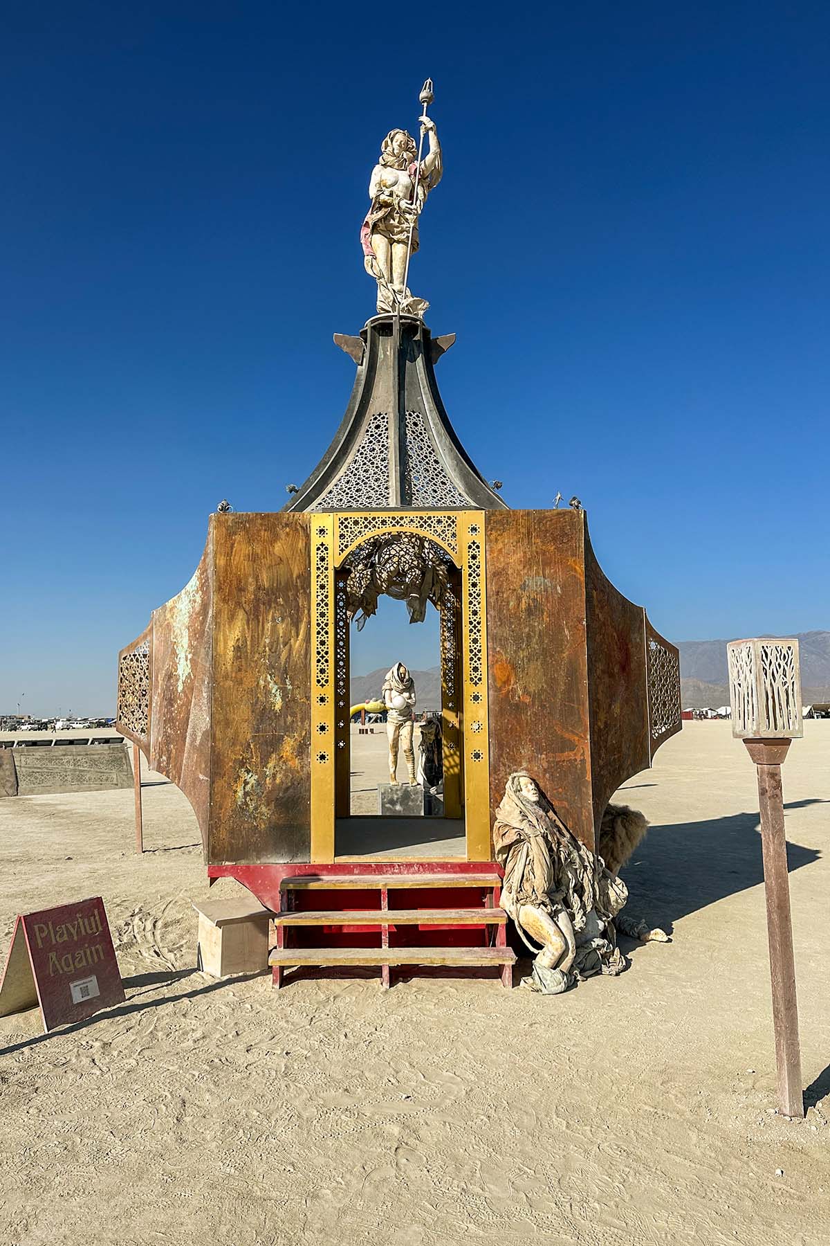 The pavilion's gold-framed doorway and red steps in bright daylight, with a kneeling figure beside it