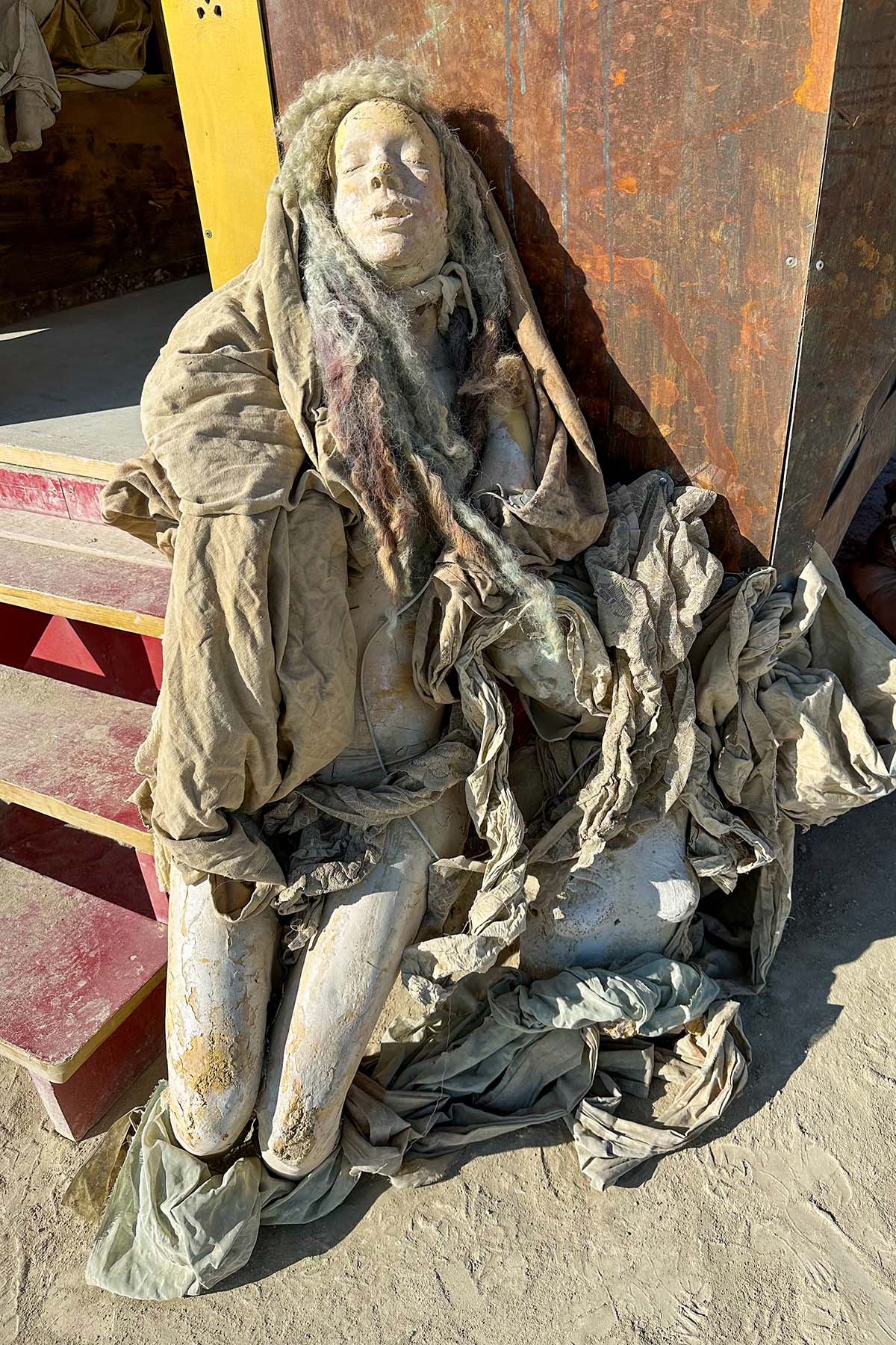 Close-up of a cloth-draped sculpture with a pale face resting against the pavilion steps