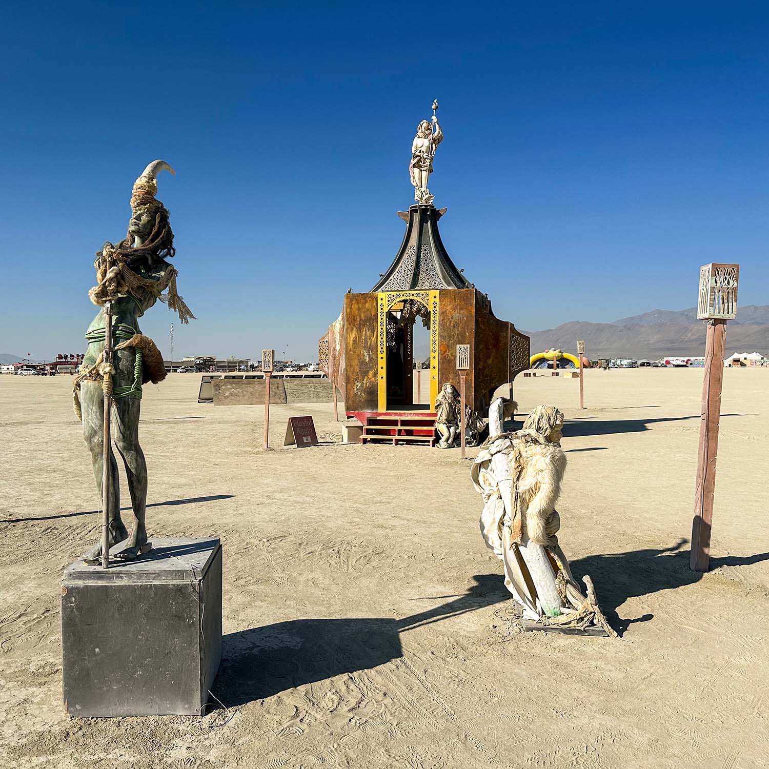 The horned figure on a plinth and a crouching sculpture in front of the pavilion in bright sun