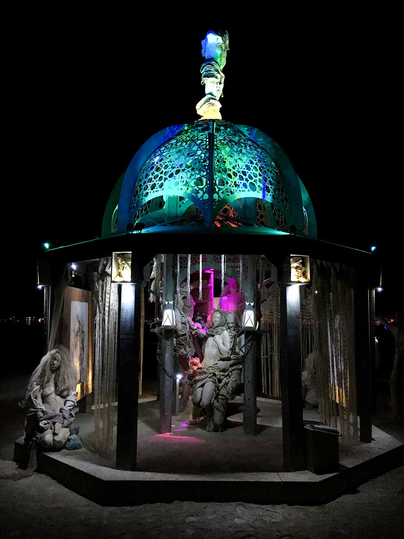Front view of the structure at night, the embracing figures lit in magenta beneath the glowing green dome