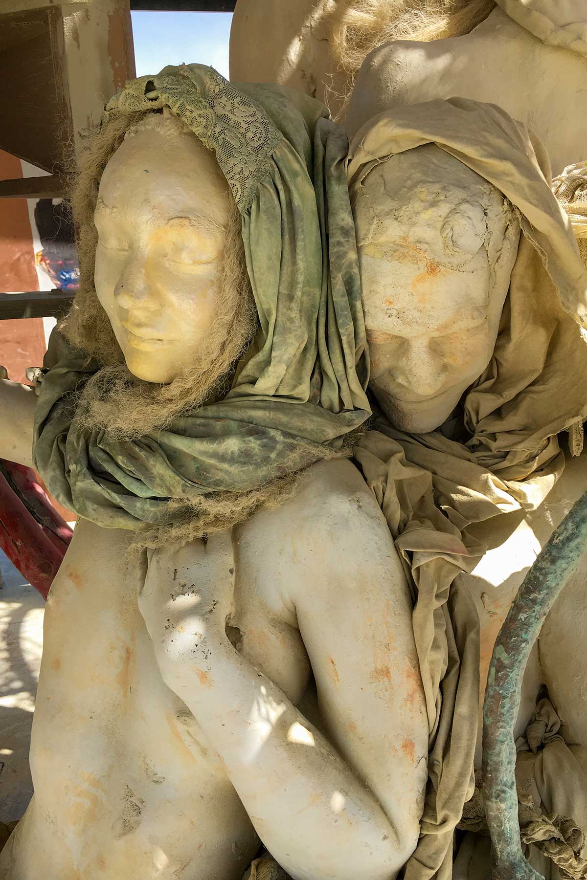 Close-up of the embracing pair by day: the woman in a green headscarf, the second figure resting its face against her