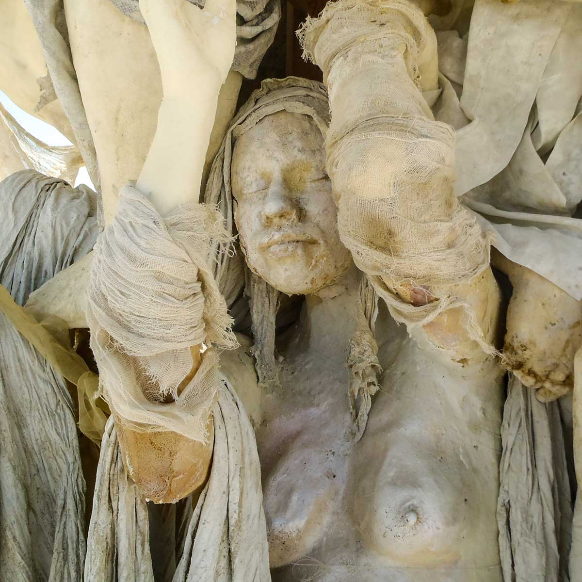 Close-up of a cast woman's serene face with closed eyes, framed by fabric-wrapped arms hanging from the branches above