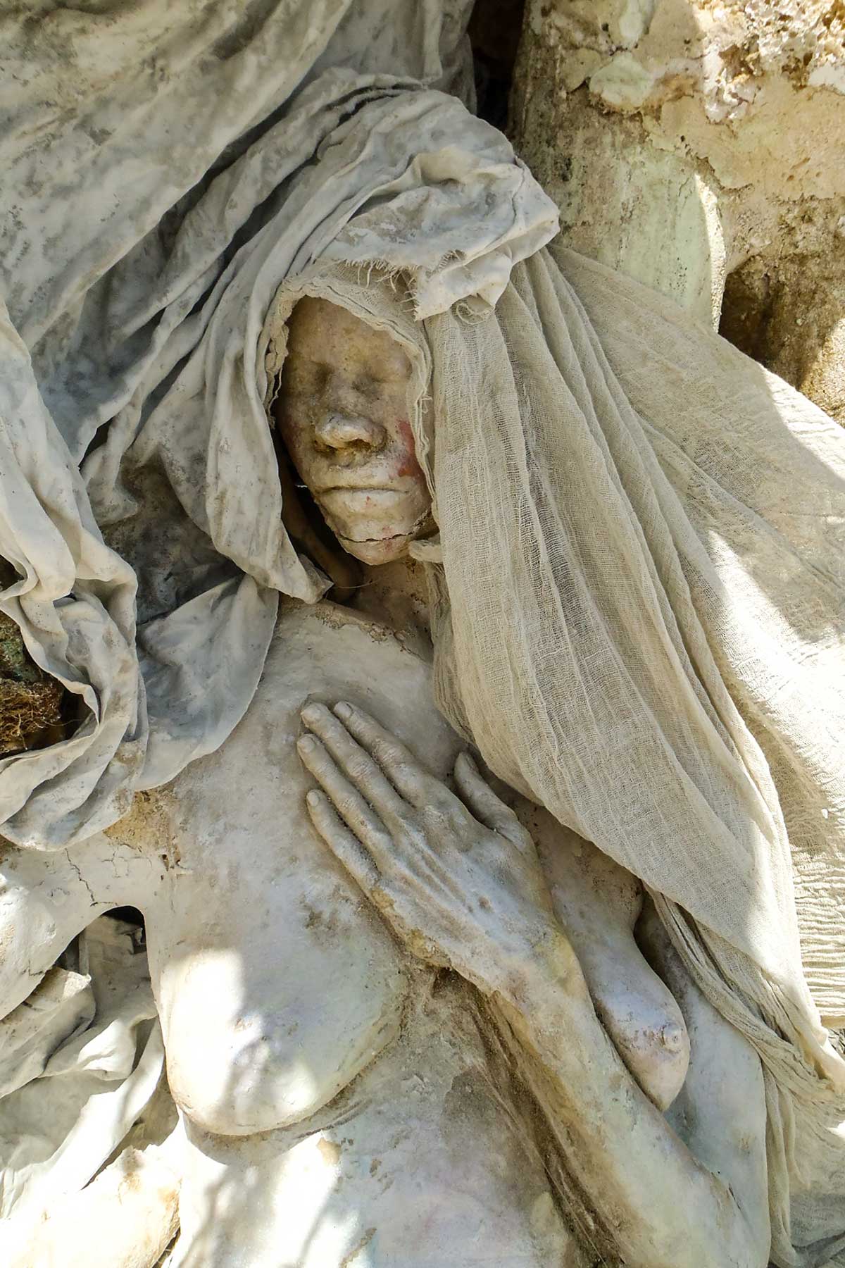 Close-up of a veiled cast figure in shade, eyes closed and one hand pressed to her chest