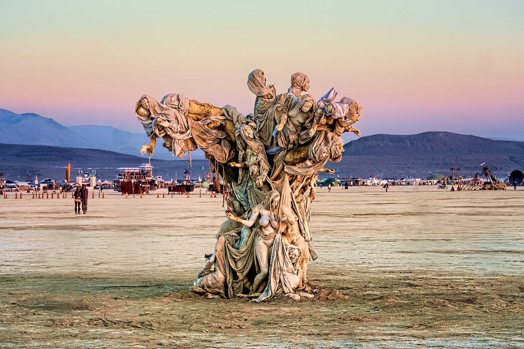 Womantree at dusk under a pink and lavender sky, framed by wooden posts with distant mountains behind