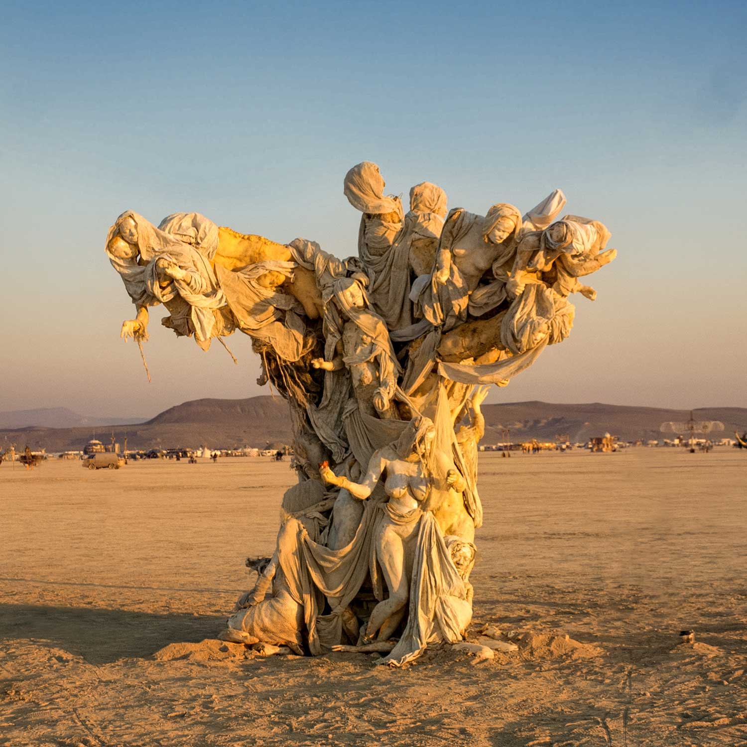 Womantree in warm golden-hour light on the open playa, with distant mountains on the horizon