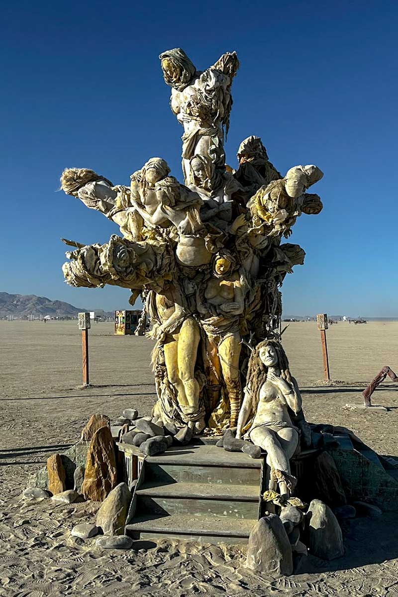 Womantree in morning light, with a cast figure of a woman seated at its base beside the steps