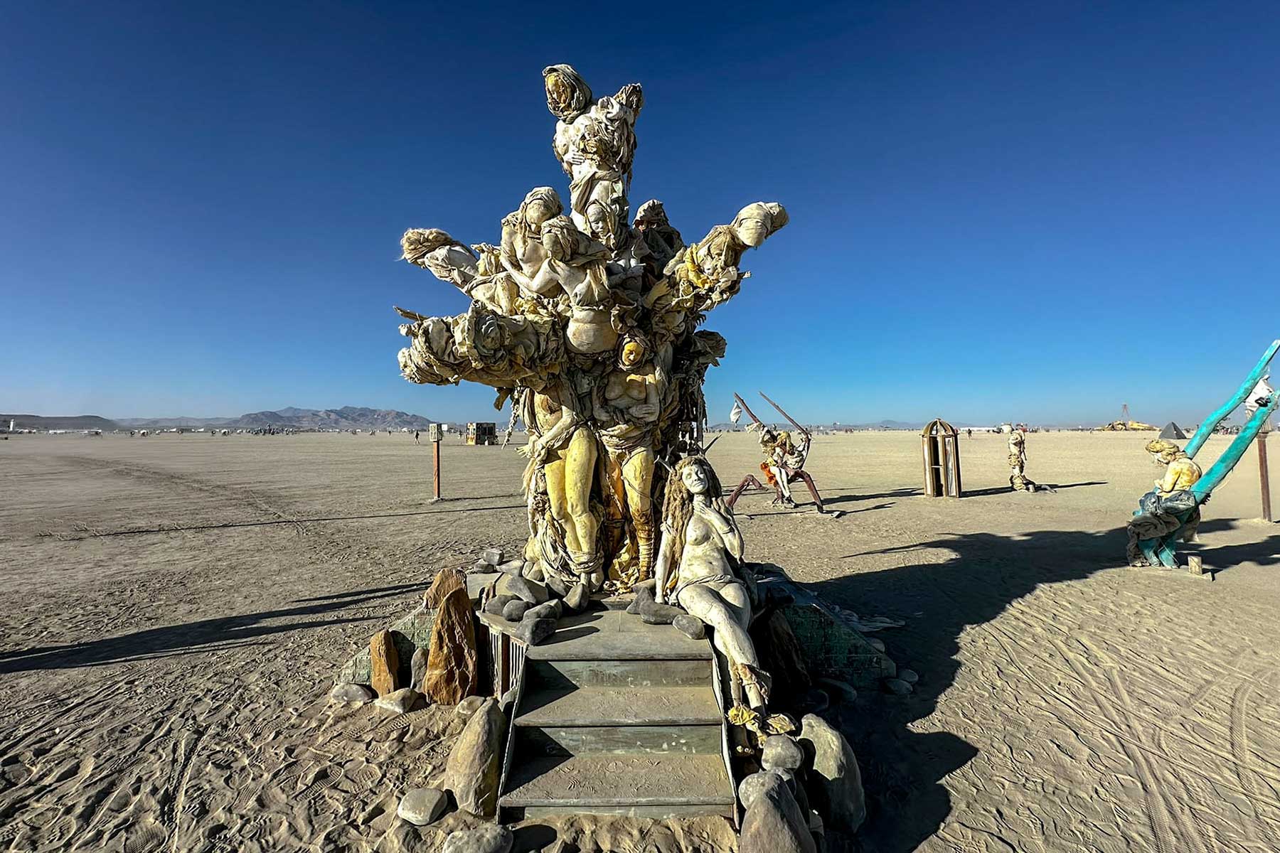 Wide view of Womantree and its stone steps on the open playa, with a teal swing sculpture nearby