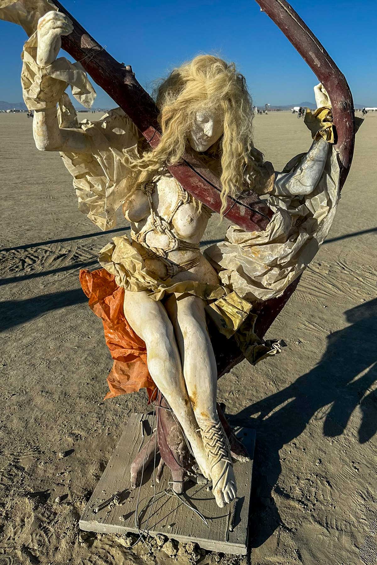Cast figure of a woman with blond hair and an orange skirt sitting on a swing