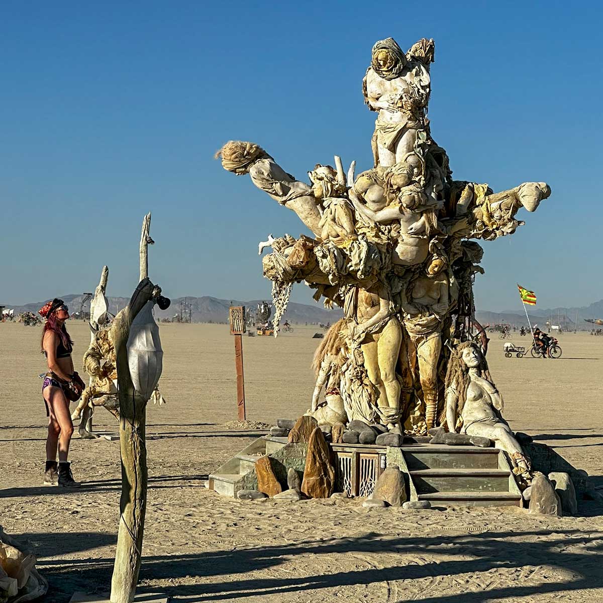 A visitor stands beside a cast figure on a post near Womantree on the playa