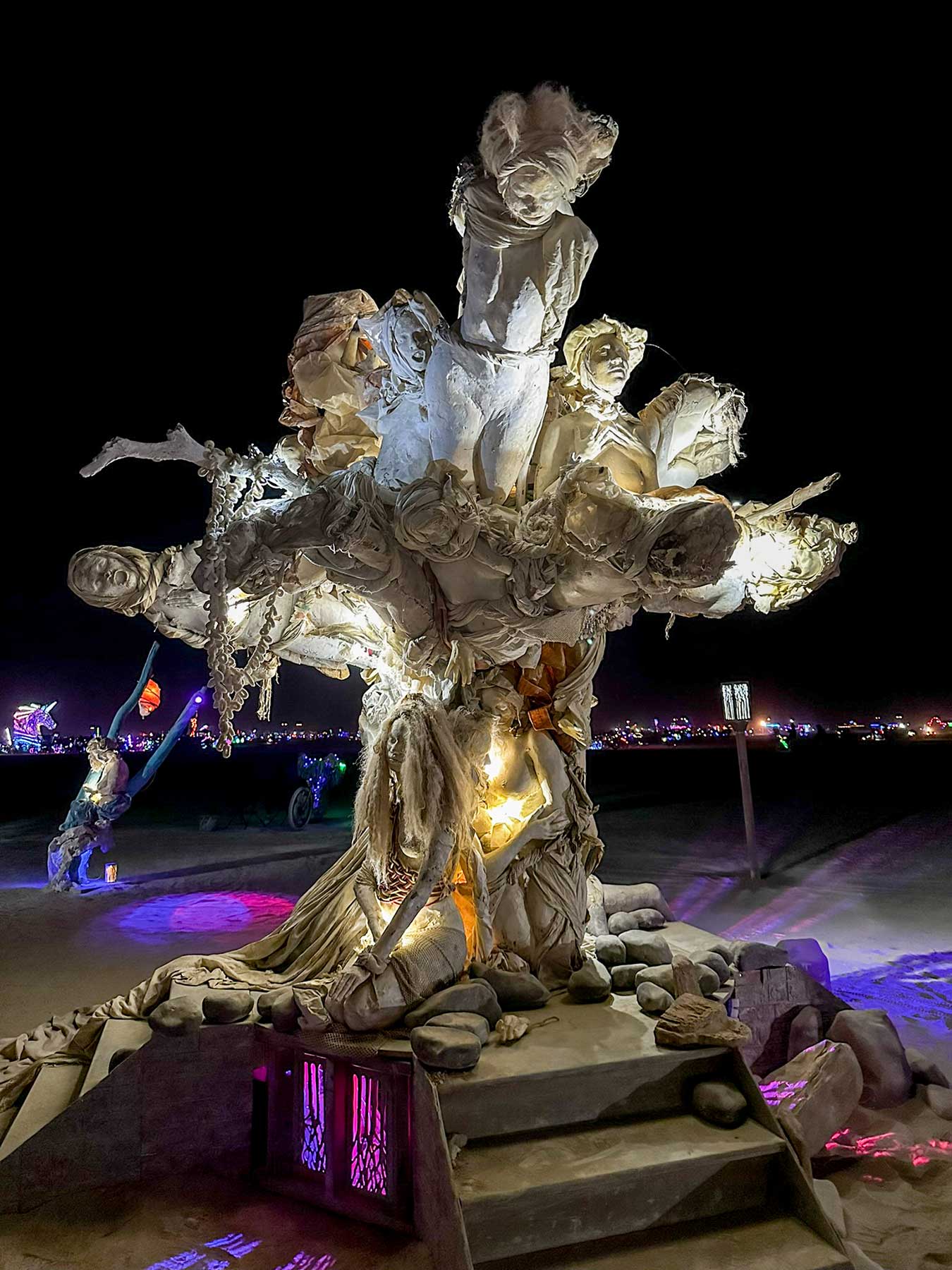 Womantree at night seen from below, light glowing through the cast figures in its branches