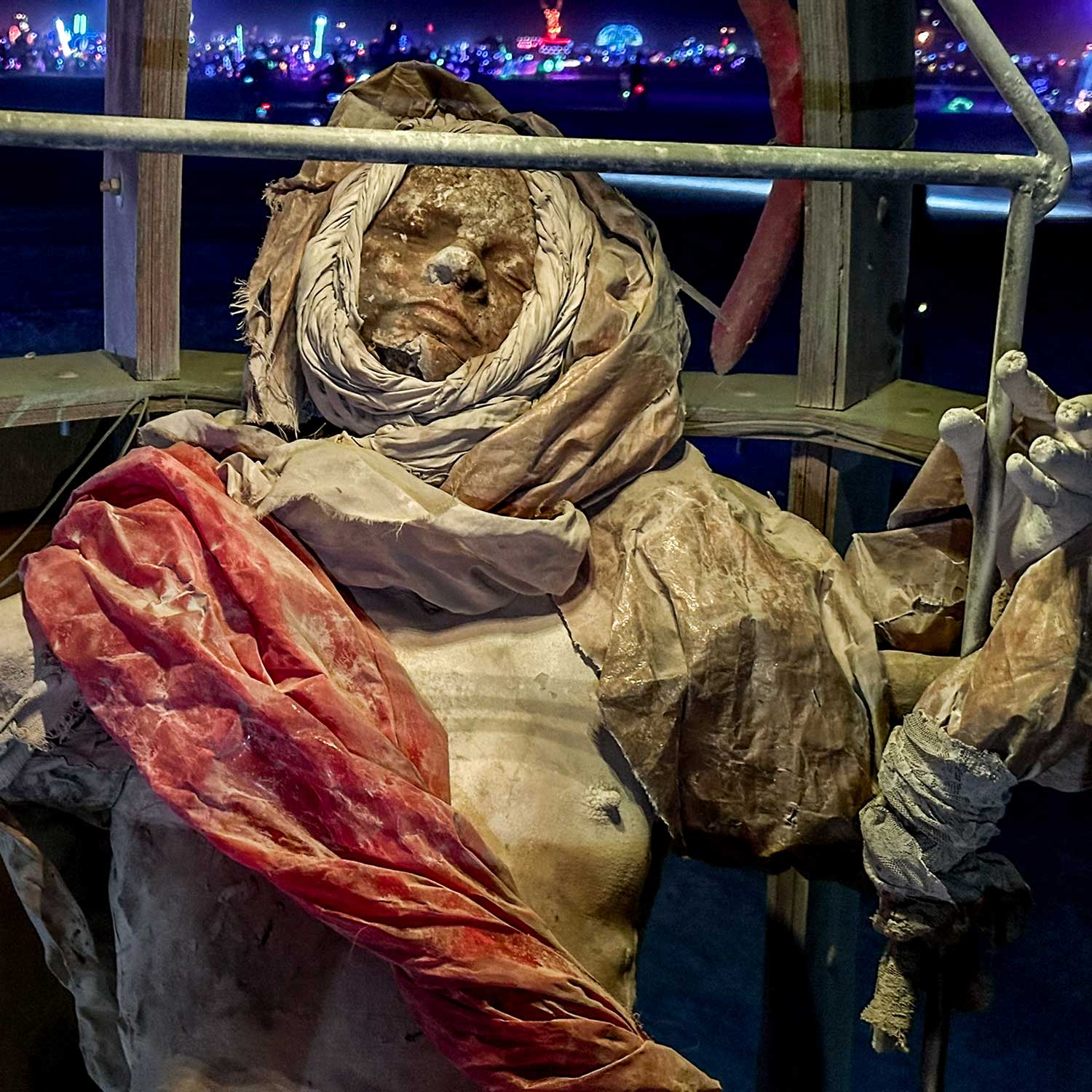 Close-up of a weathered cast figure wrapped in a hood and a red sash, at night