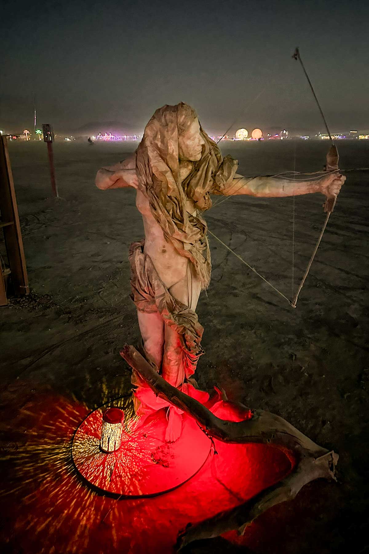 Cast figure of a woman archer drawing a bow, standing in a pool of red light at dusk