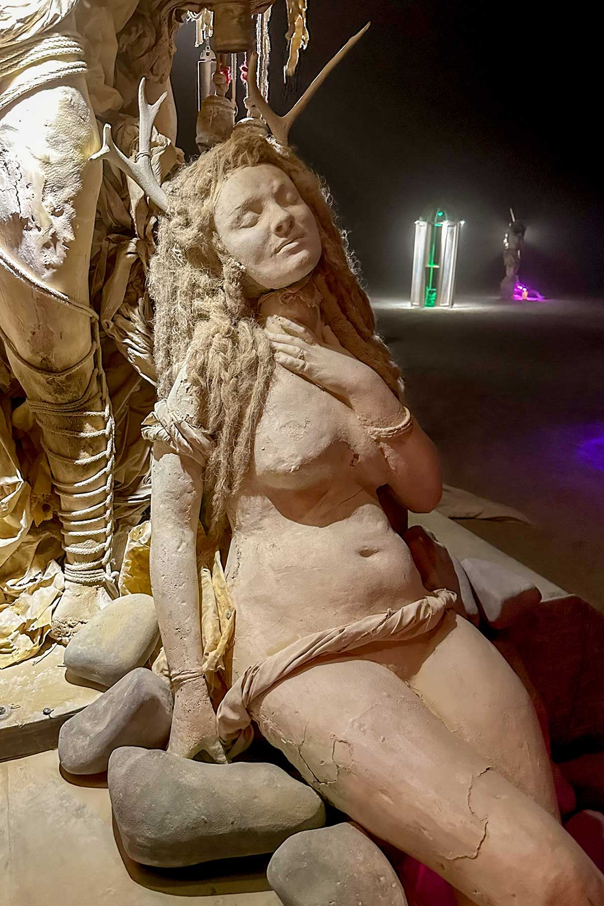 Cast figure of a reclining nude woman with long hair, resting on stones at night