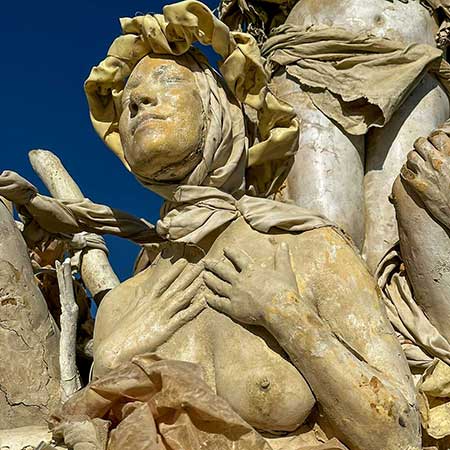 Close-up of a cast woman's face turned toward the sky, wrapped in sculpted fabric