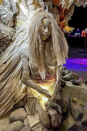 Close-up at night of a cast woman with long, pale hair, softly lit from below