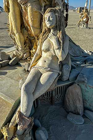 Close-up of a cast figure of a woman with long hair reclining among the stones at the base of Womantree