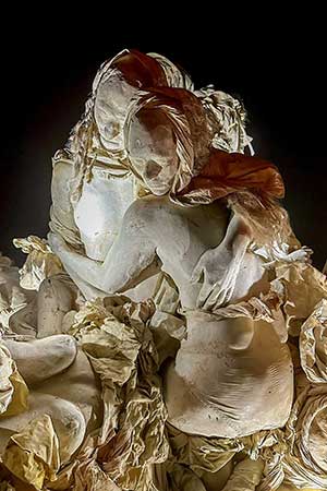 Close-up at night of two cast figures entwined in a tender embrace amid sculpted fabric