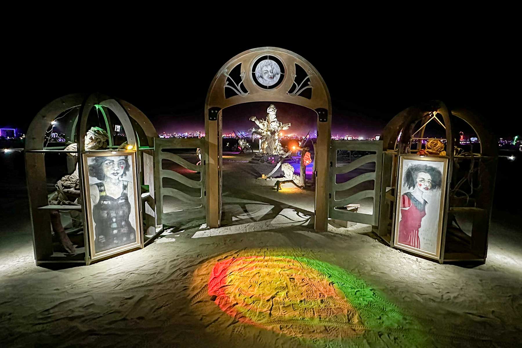 Womantree's entry gate at night: a lit arch flanked by two portrait kiosks, with colored light pooling on the ground
