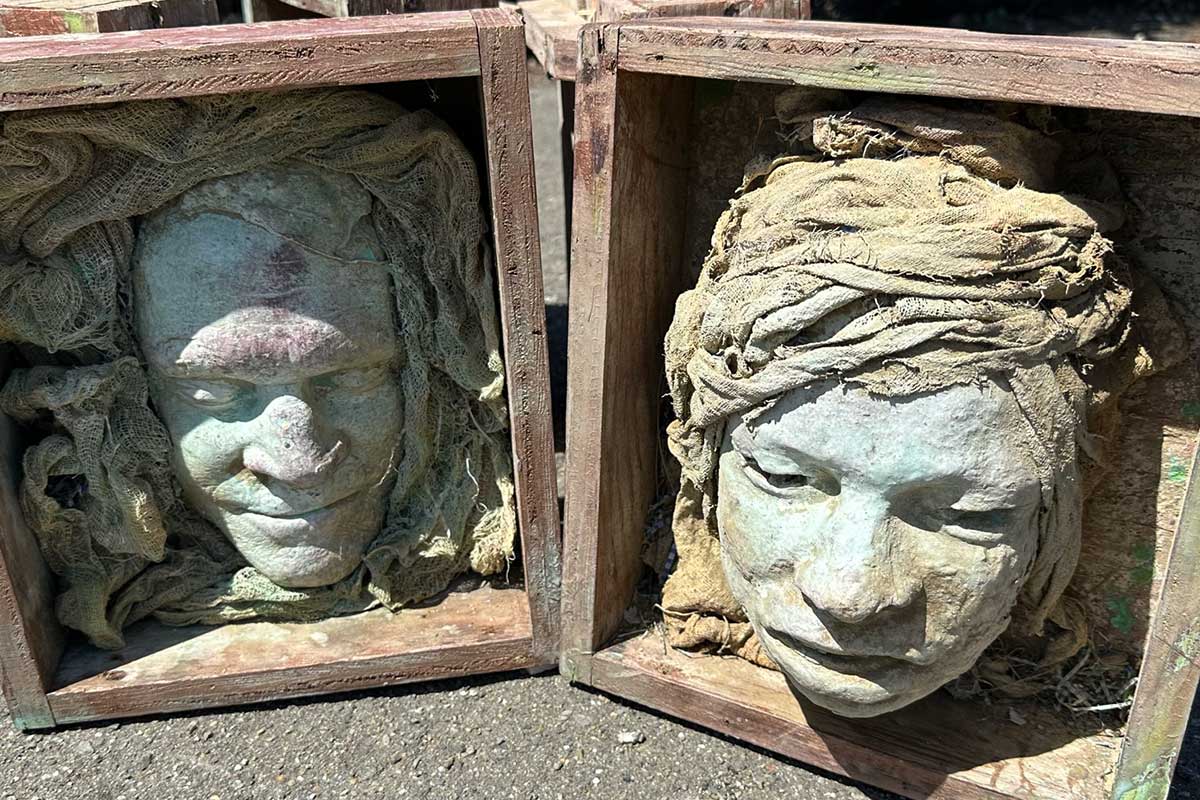 Two weathered face casts in wooden boxes, wrapped in sculpted fabric