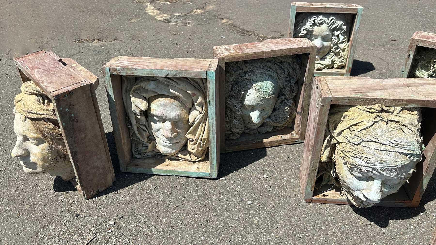 Several boxed face casts lined up on asphalt