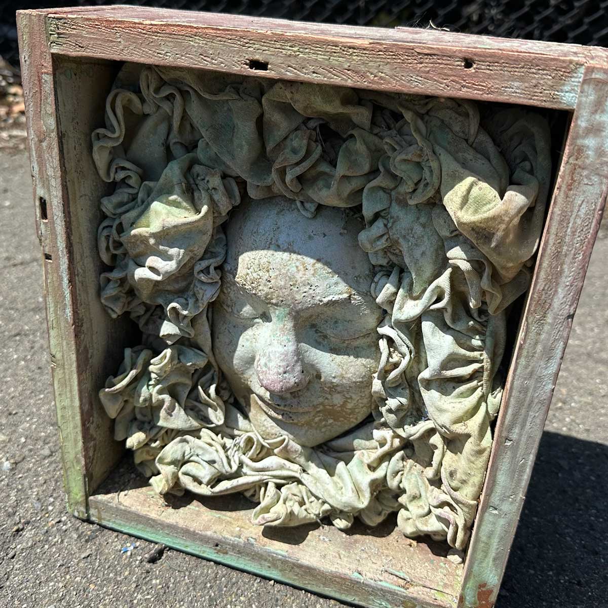 Face cast in a weathered wooden box, surrounded by ruffled, sculpted fabric
