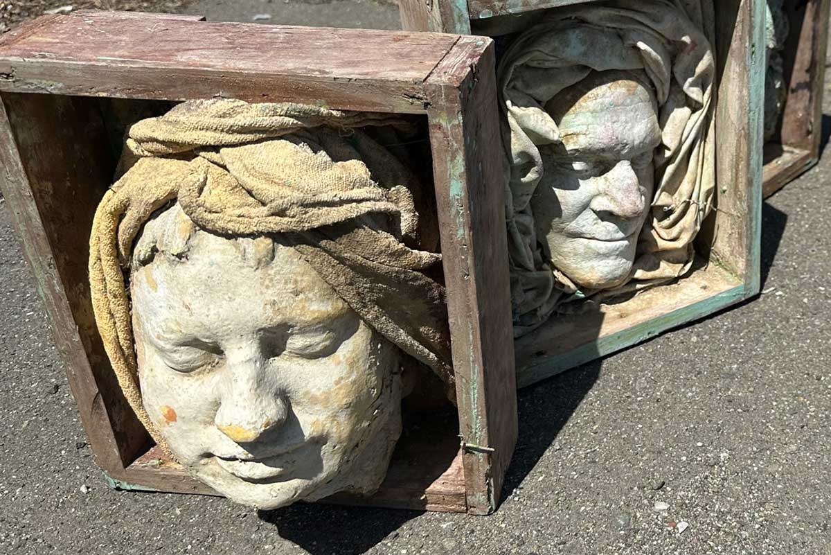 Face cast wearing a sculpted head wrap, set in a wooden box beside another boxed face