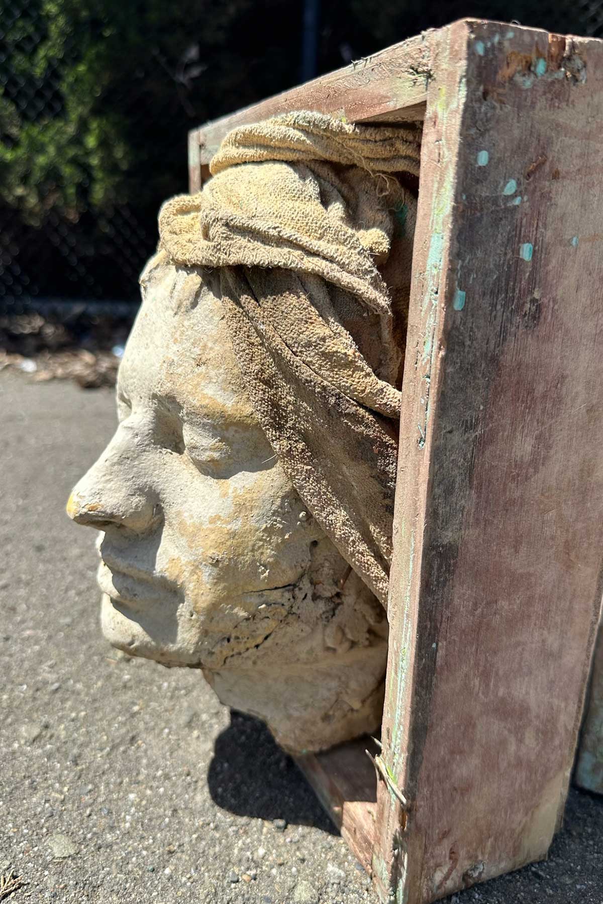 Side view of a face cast with a sculpted head wrap, set in a weathered wooden box