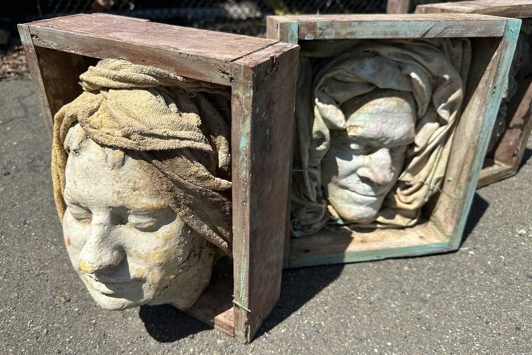 Two face casts with sculpted head wraps, set in weathered wooden boxes