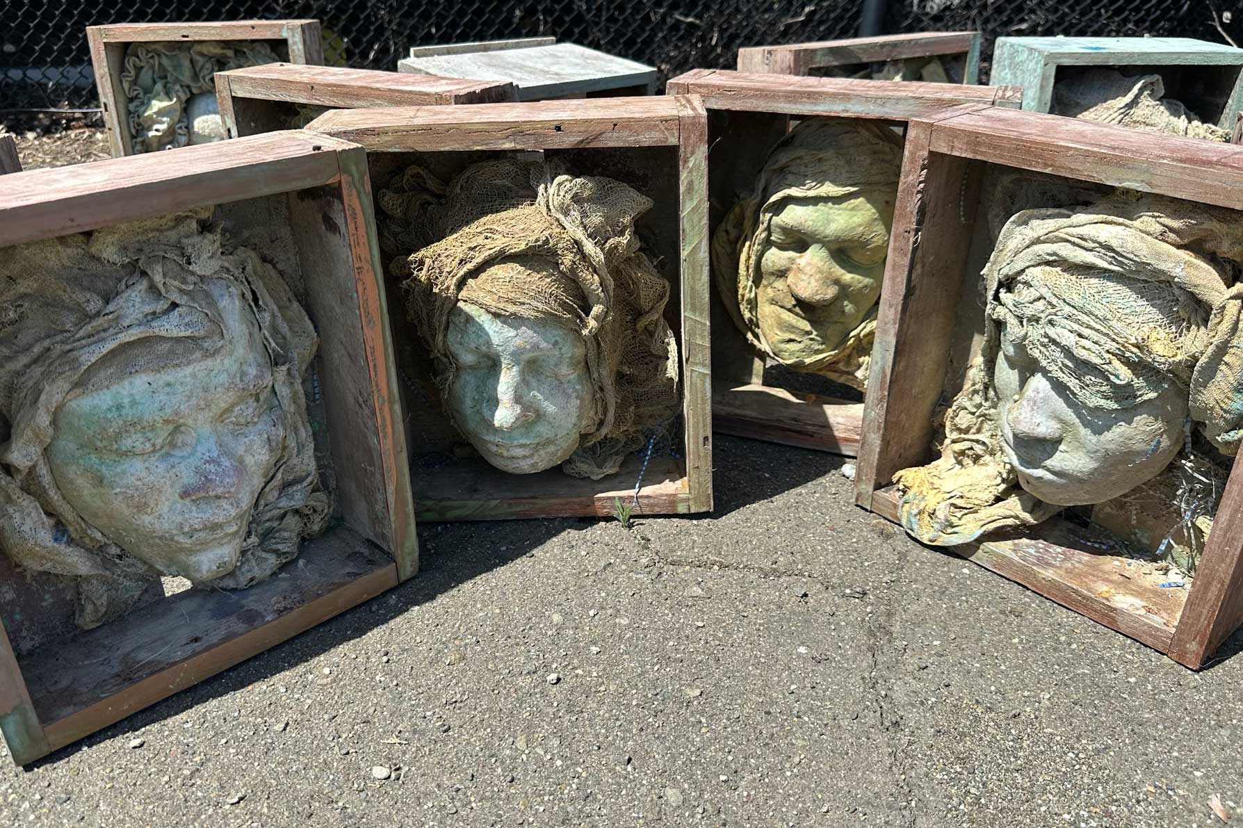 Row of weathered boxed face casts on asphalt