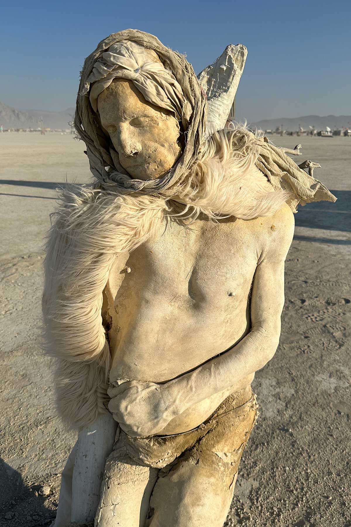 Cast figure in a fur-trimmed wrap, standing on the playa in early light