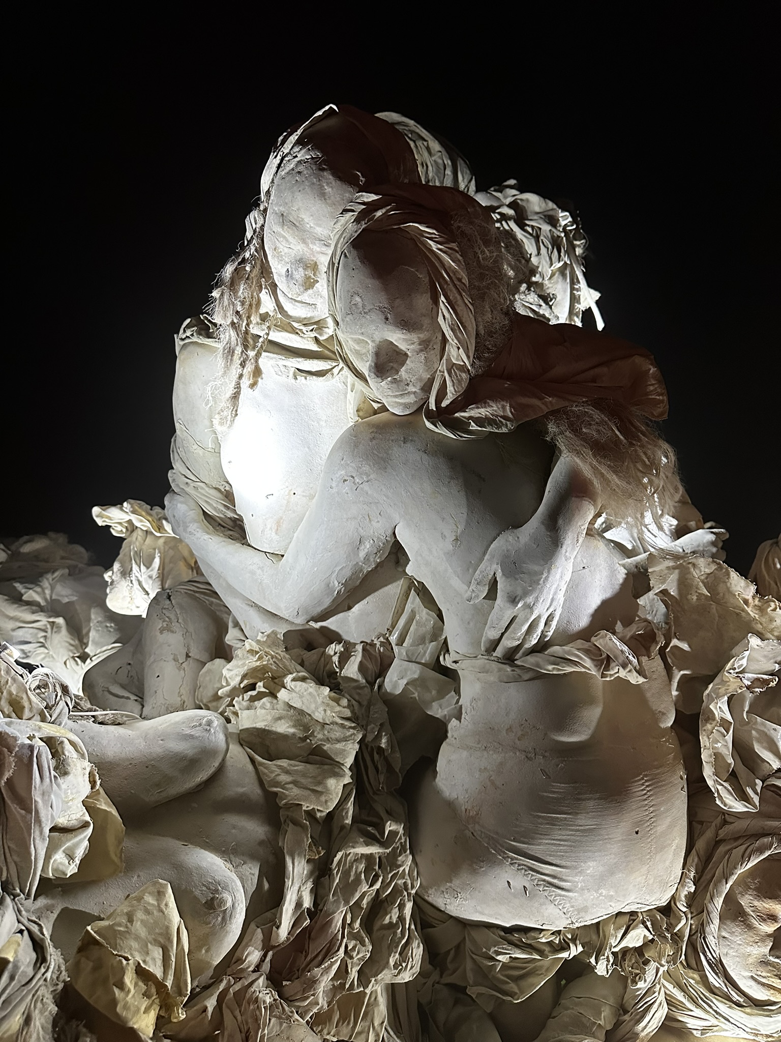 Two embracing cast figures lit against the night sky, surrounded by sculpted fabric